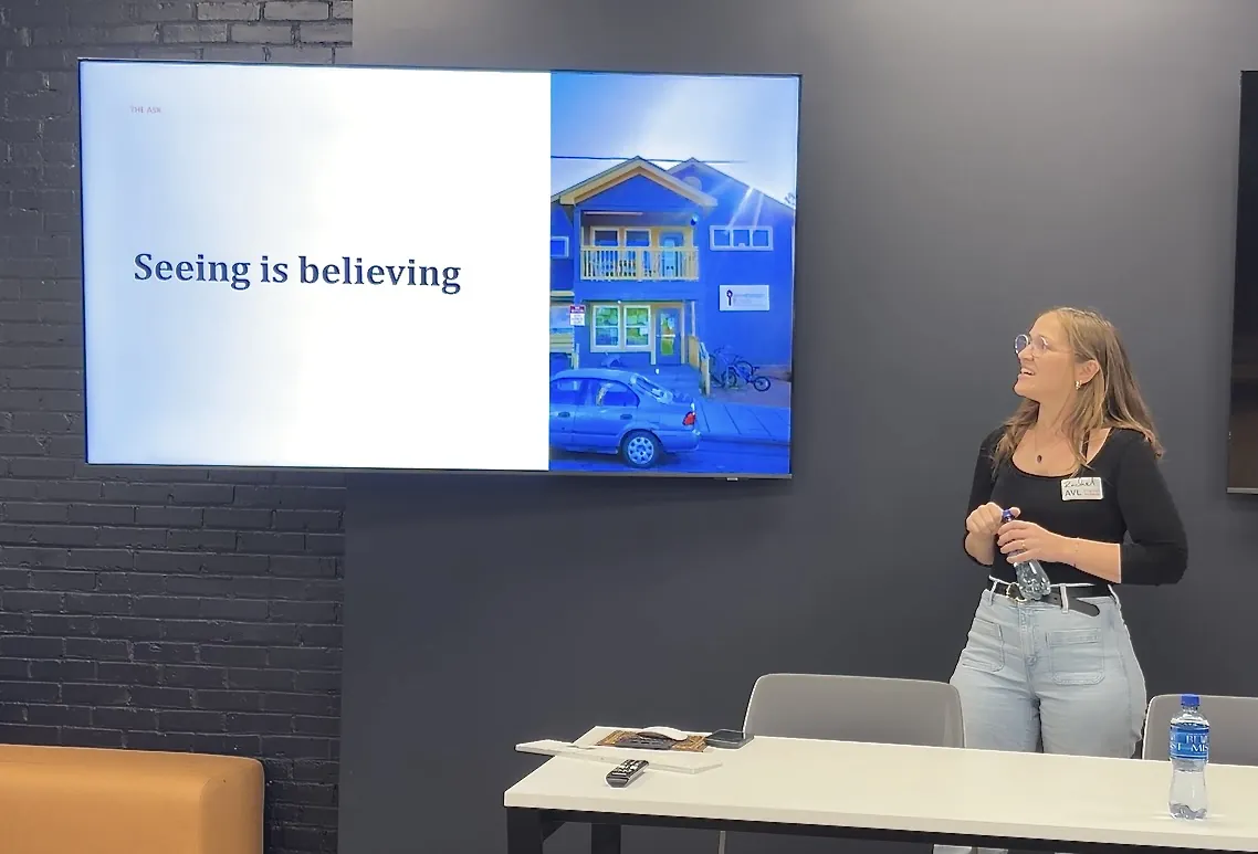 A presenter standing beside a screen showing a slide titled &ldquo;Seeing is believing&rdquo;, at an AVL UX meetup