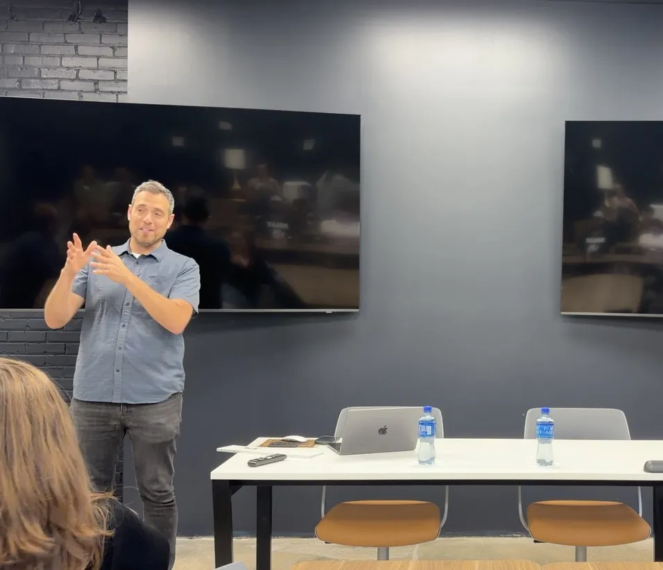 A speaker gesturing mid-talk in front of two wall-mounted screens, at an AVL UX meetup