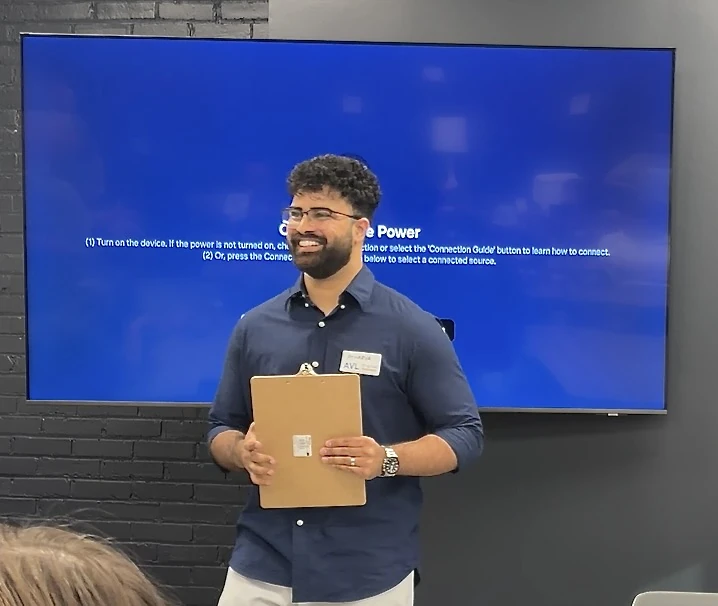 Atharva Dnyanmote holding a clipboard in front of a presentation screen